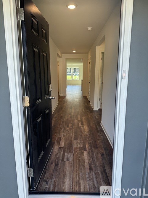 A hallway with wood flooring and a black door on the left.