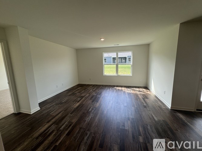 A room with wooden flooring and a window overlooking a grassy area.