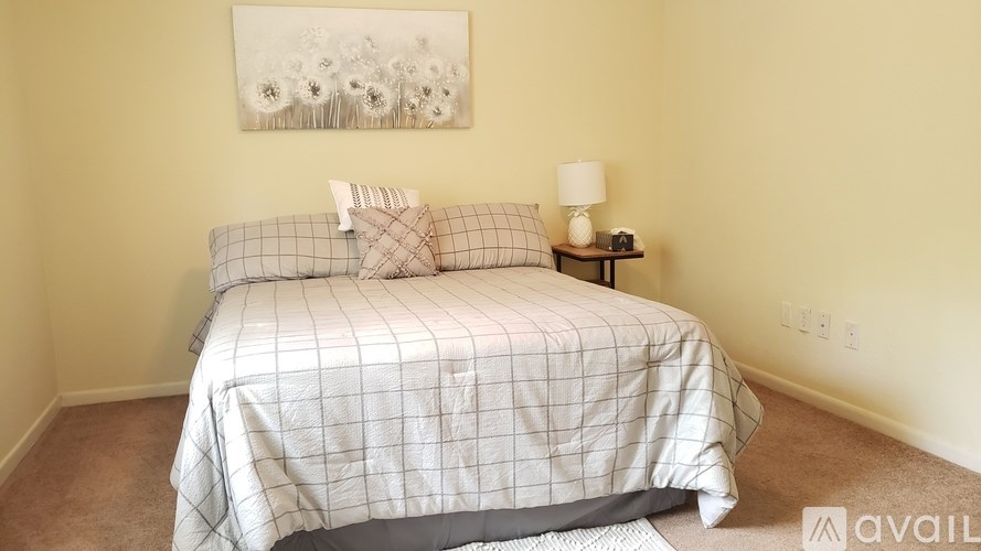 A bedroom with a bed, pillows, a lamp, and a painting on the wall.