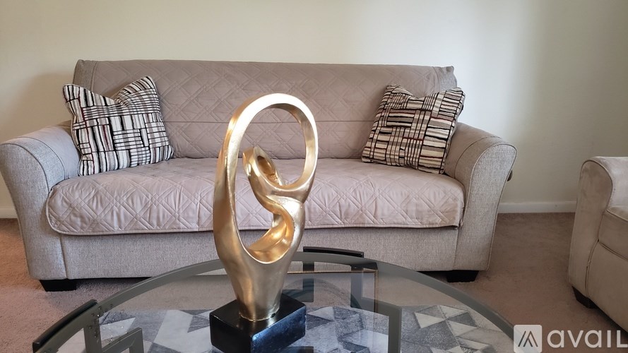 A modern living room with a grey couch and a metallic sculpture on a glass table.