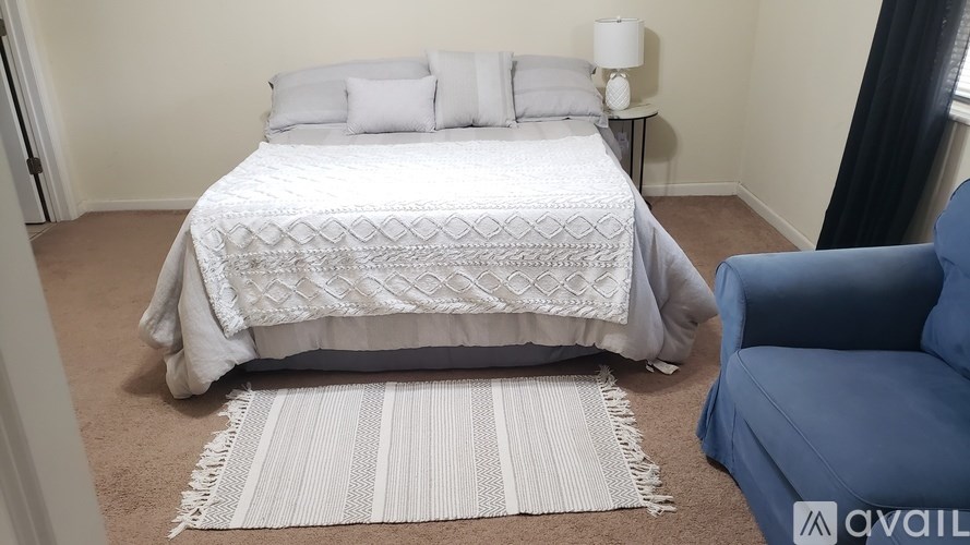 A bedroom with a white bedspread and a blue chair.