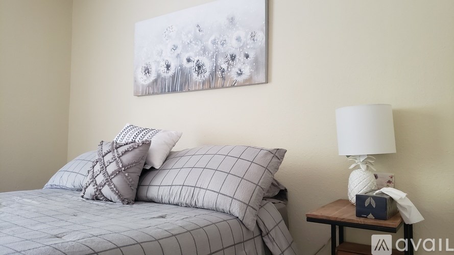 A bed with a grey and white striped comforter and two matching pillows sits next to a small table with a lamp and a tissue box.