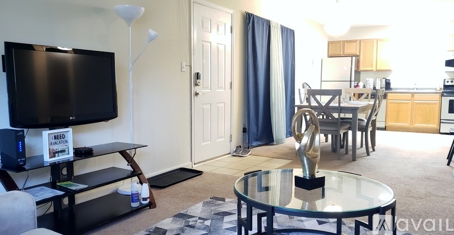 A living room with a television, a glass table, and a dining area in the background.