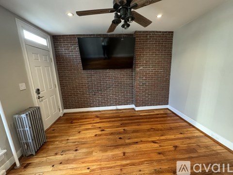 A room with a wooden floor and a brick wall with a flat screen TV mounted on it.