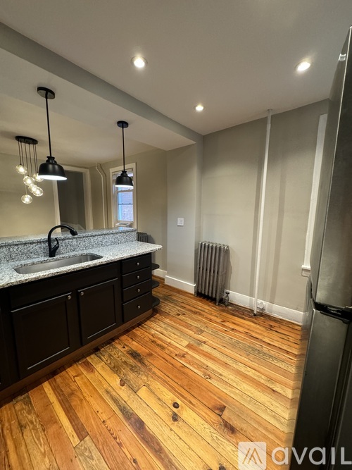 A kitchen with wooden floors and a black fridge.