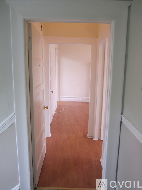 A hallway with white walls and wood flooring.