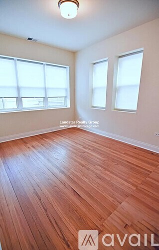A room with wooden flooring and two windows.