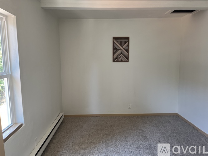 A carpeted room with a picture on the wall and a window on the left.
