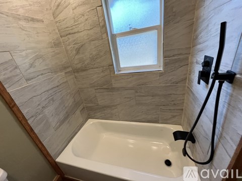 A white bathtub with a window above it in a bathroom.
