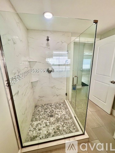 A shower with a glass door and a marble floor.