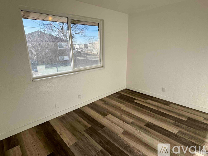 A room with wooden flooring and a window overlooking a residential area.