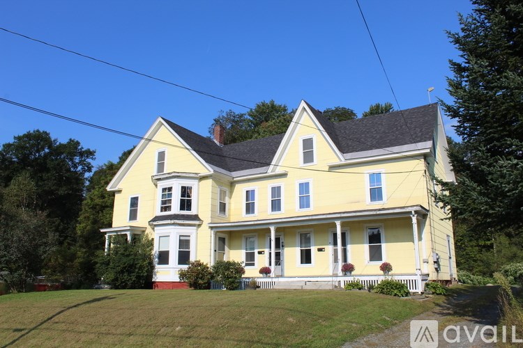 A yellow house with a red door and a white porch.