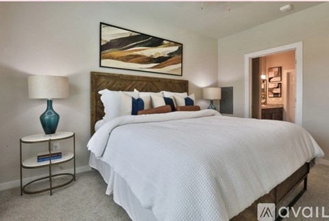 A bedroom with a large bed, a nightstand with a lamp, and a painting on the wall.