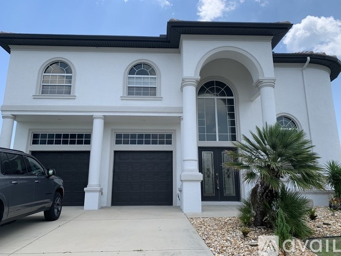 A white house with a black garage door and a grey car parked in front.