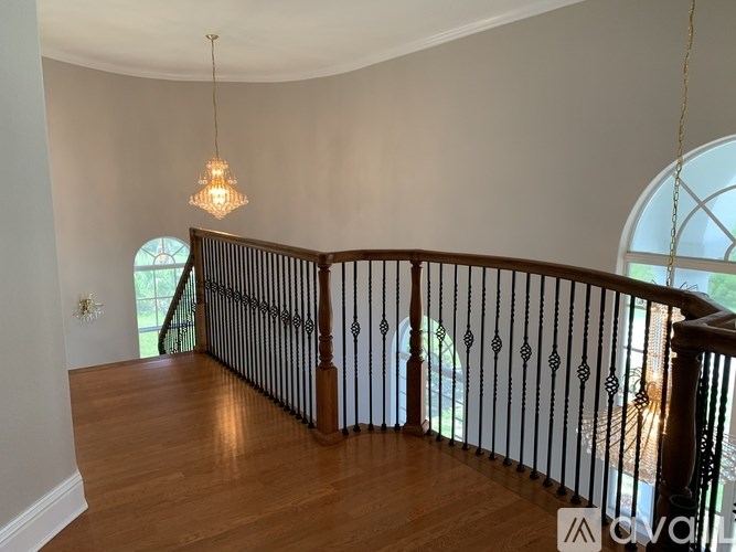 A chandelier hangs from the ceiling in a room with a wooden floor and a balcony with a metal railing.