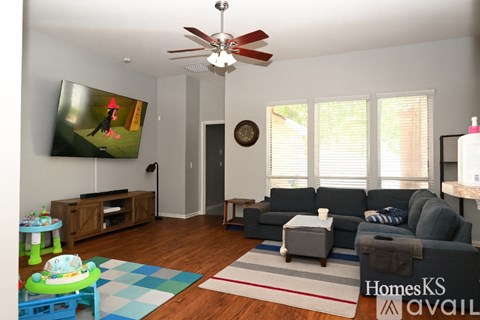 A living room with a grey couch, a blue and white rug, and a television on the wall.