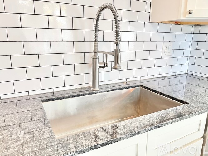 A kitchen sink with a chrome faucet and a white tile backsplash.