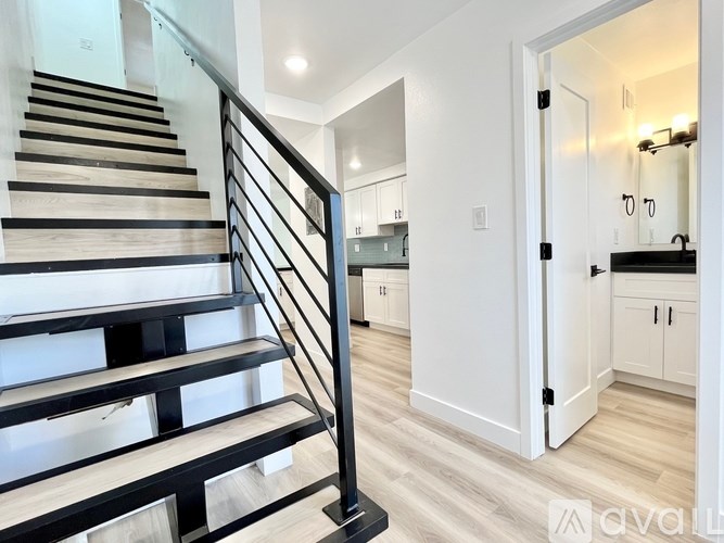 A staircase with a black metal railing and wooden steps leads to a kitchen area.
