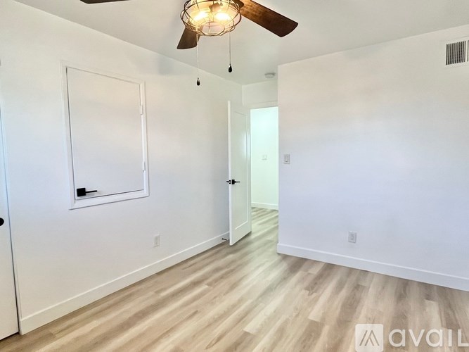 A room with a ceiling fan and light, a door, and a window with a white frame.