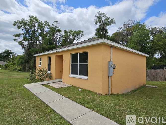 A small yellow house with a grey roof and a grey walkway leading to the front door.