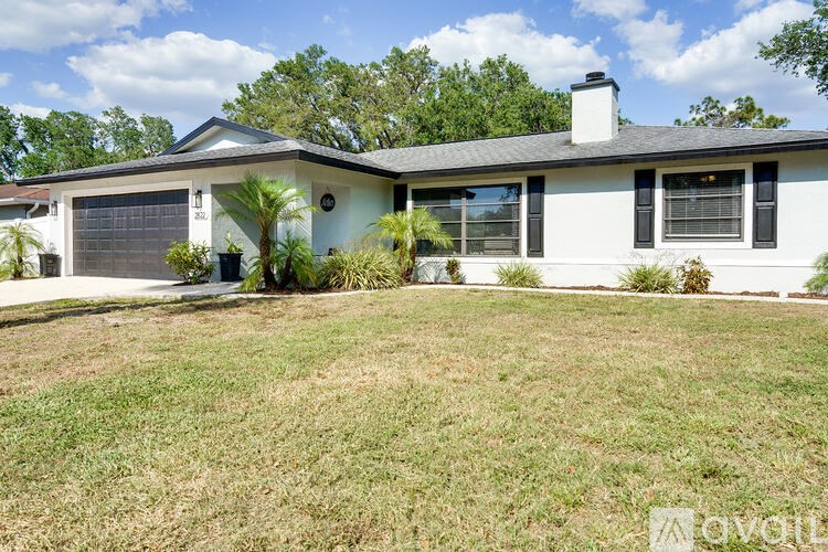 A white house with a black roof and a chimney is surrounded by a grassy lawn.