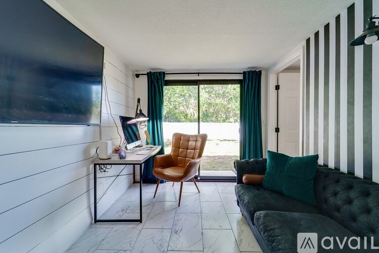 A living room with a black couch, a desk with a computer, and a chair.