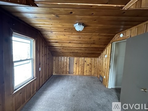 A room with wooden walls and ceiling, a window, and a carpeted floor.