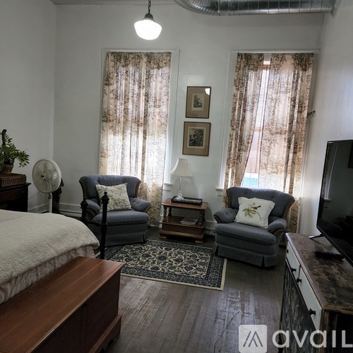 A bedroom with a bed, two chairs, and a table with a lamp on it.