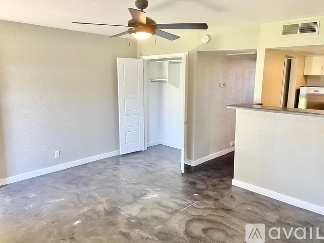 A room with a ceiling fan and a kitchenette in the background.