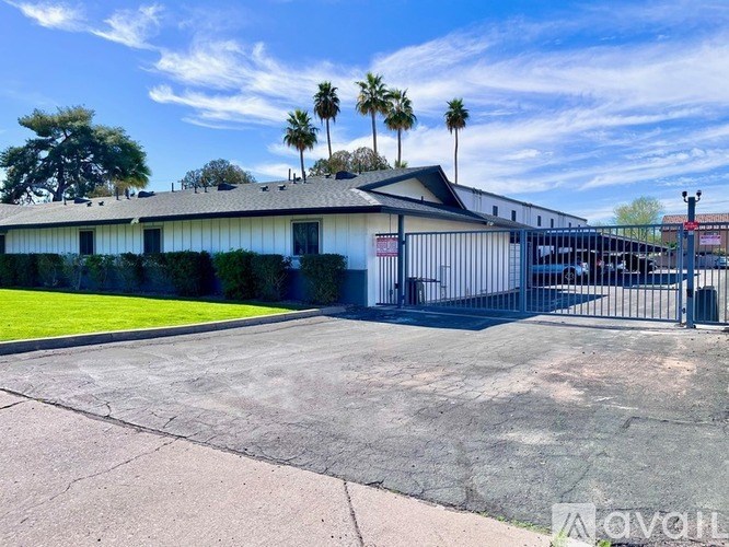A building with a white facade and a black roof is surrounded by a fence and palm trees.