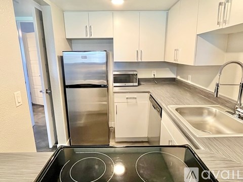 A kitchen with a stove top oven in the foreground and a refrigerator, microwave, dishwasher, and sink in the background.