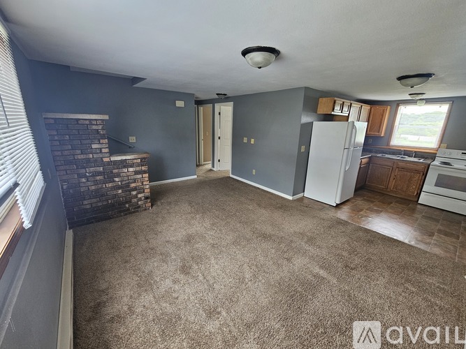 A living room with wooden floors and a kitchen area in the background.