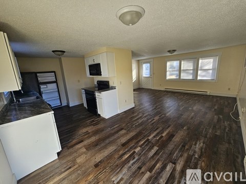 A living room with wooden floors and a kitchen area in the background.