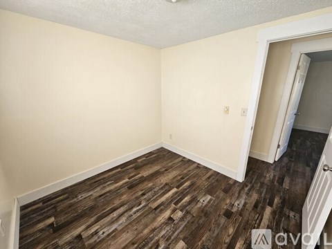 A room with wooden flooring and a doorway leading to another room.