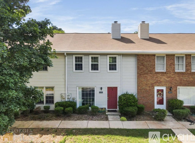 A house with a red door and white siding is surrounded by greenery.