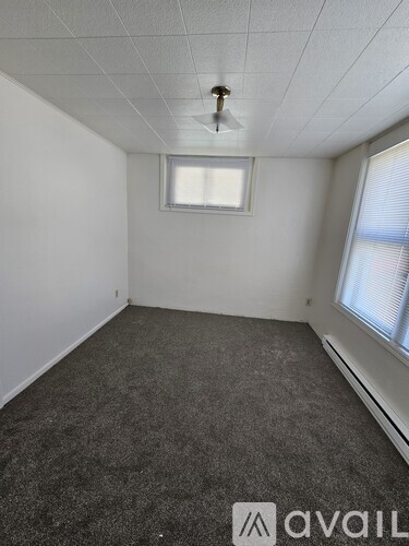 A room with grey carpet and a window with blinds.
