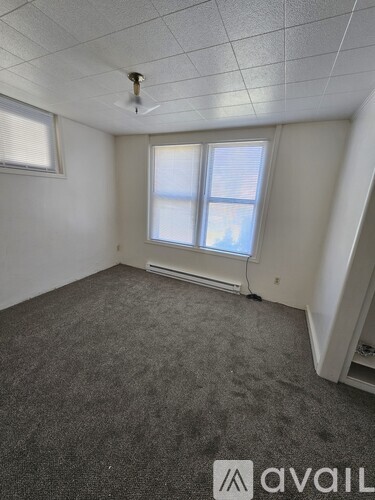 A room with a carpeted floor, a window with blinds, and a ceiling fan.
