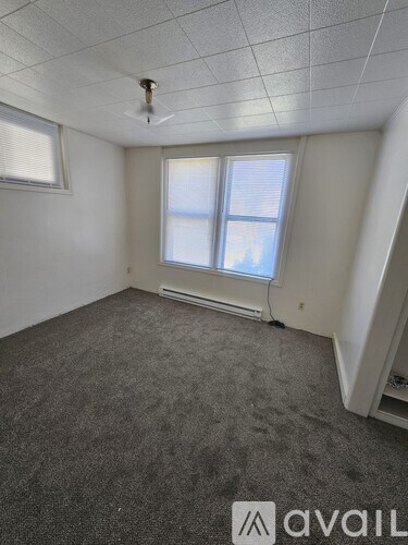 A room with a carpeted floor, a window with blinds, and a ceiling fan.