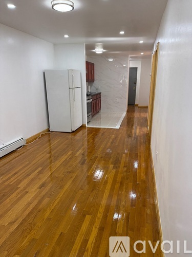 A long hallway with wooden floors and a white refrigerator.