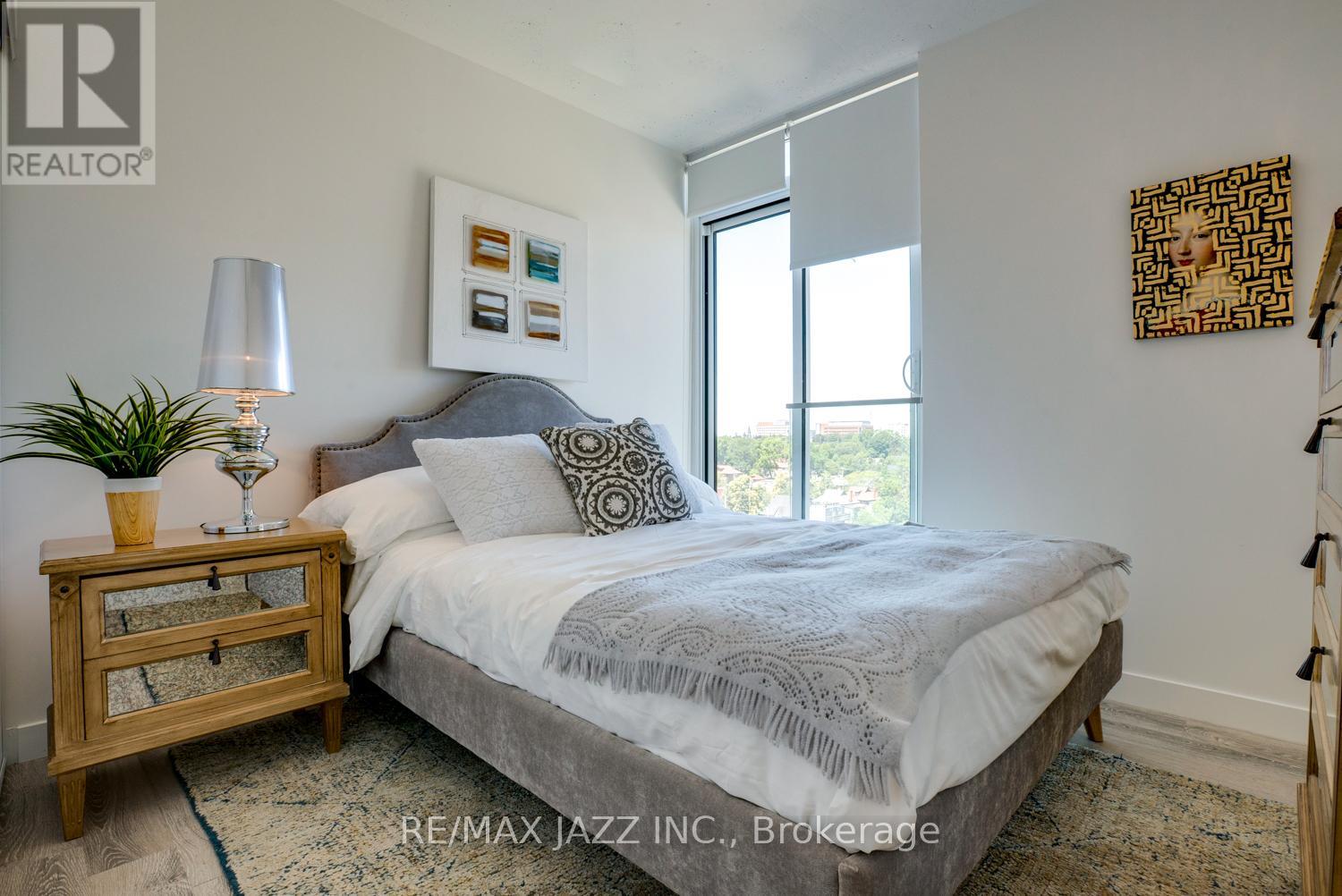 A bedroom with a bed, nightstand, lamp, and artwork.