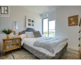 A bedroom with a bed, nightstand, lamp, and artwork.
