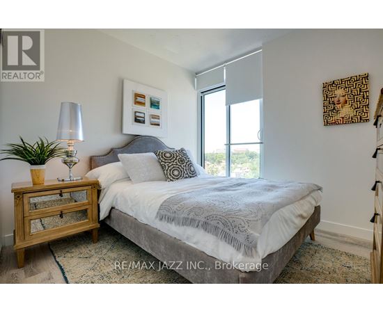 A bedroom with a bed, nightstand, lamp, and artwork.
