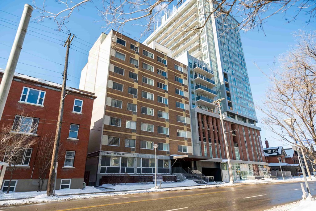 A tall building with a glass facade stands next to a shorter brick building.