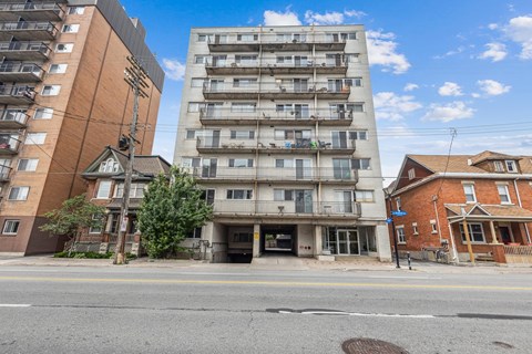A street view with apartment buildings and a blue sky with clouds.