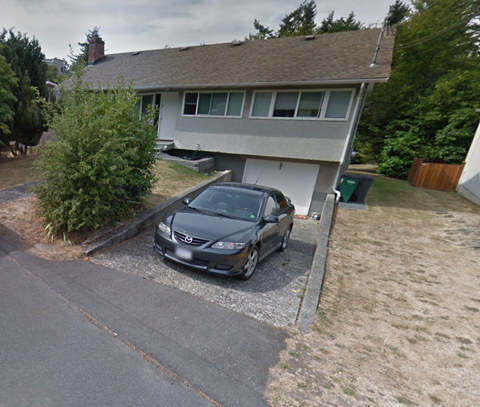 A gray car is parked in front of a house.