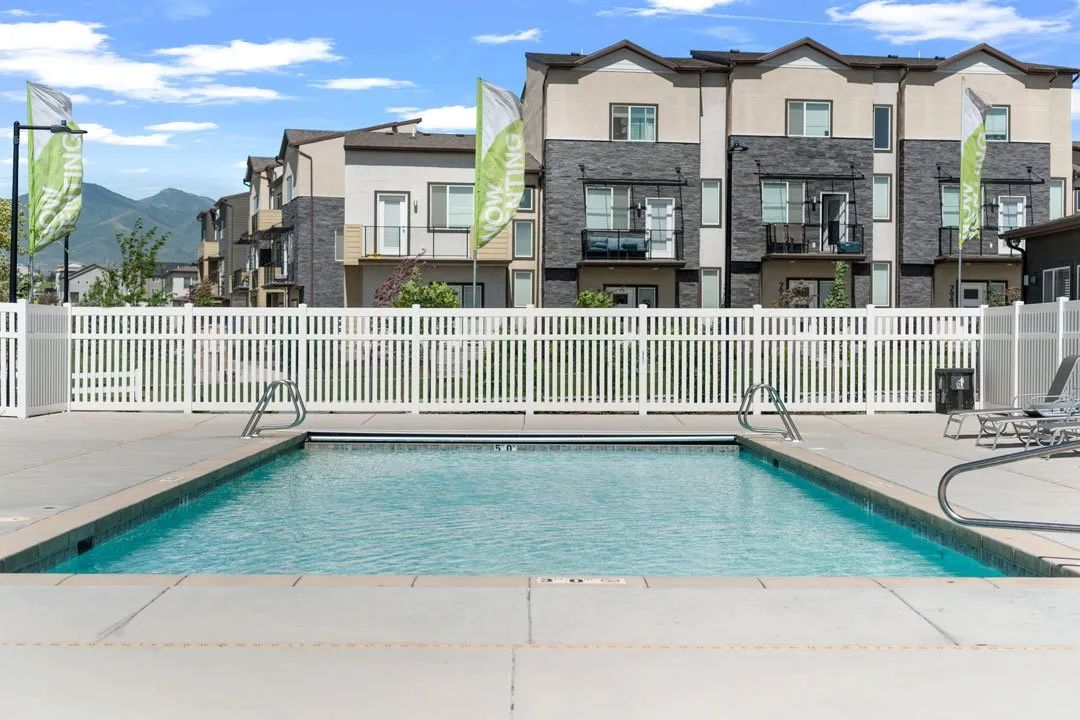 A pool in front of apartment buildings with flags on the fence.
