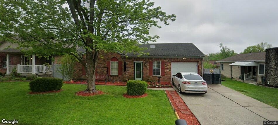 A white car is parked in front of a brick house.