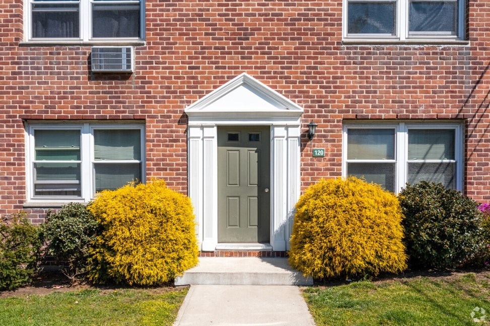 A red brick house with a white door and two green bushes on either side.