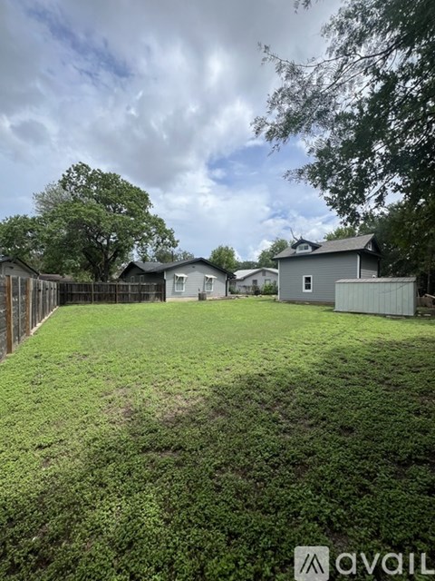 A grassy backyard with a fence and houses in the background.