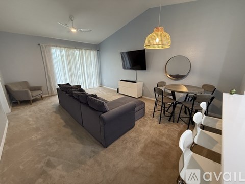 A living room with a grey sofa, a television, a dining table with chairs, and a ceiling fan.